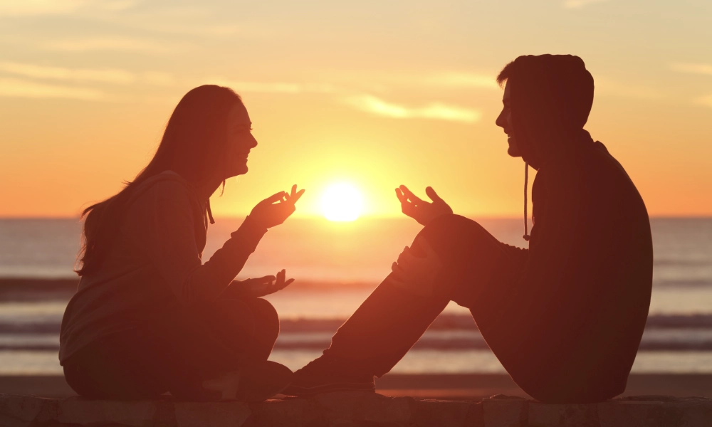 Two people sitting together talking in front of a sunset